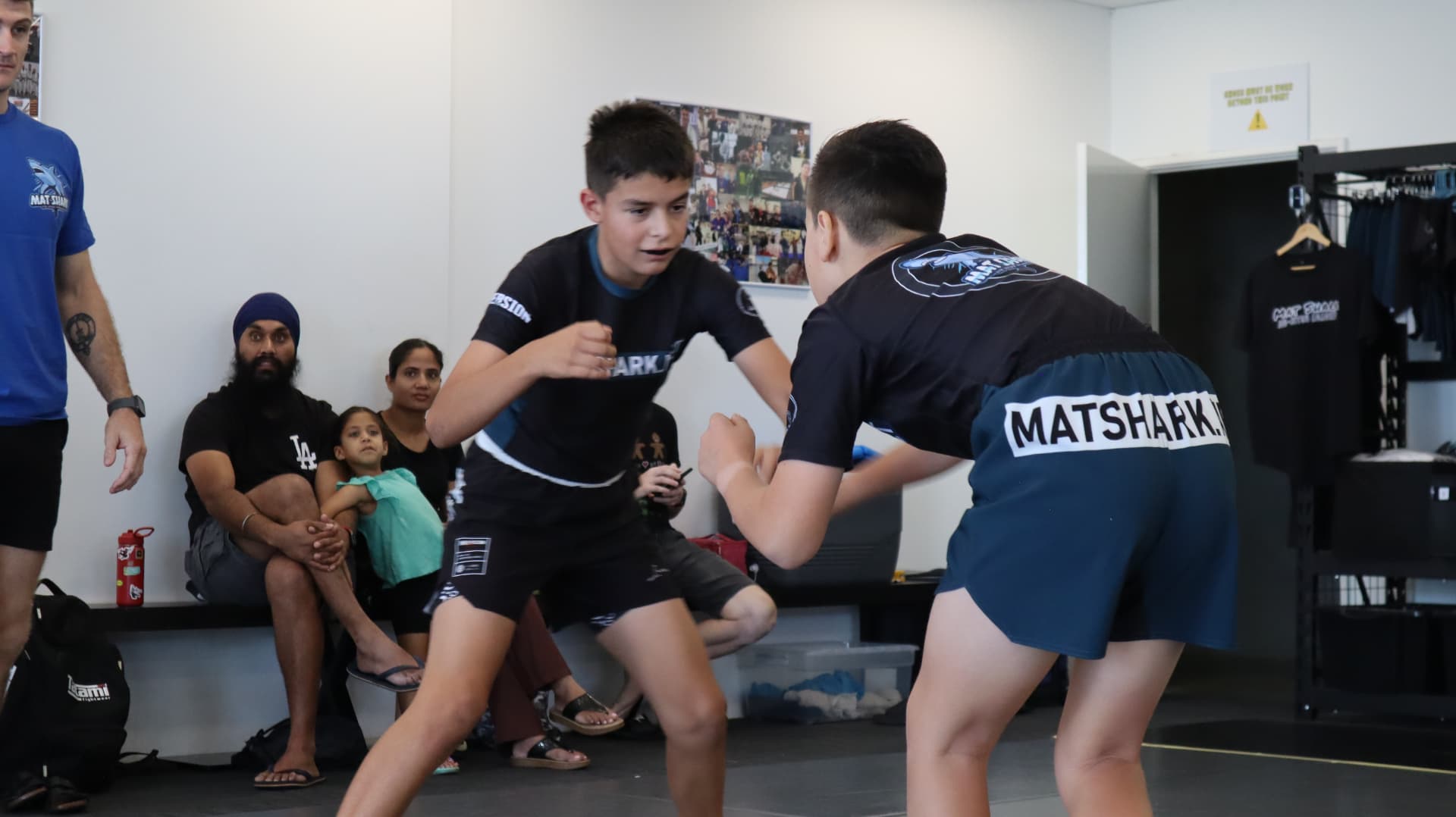 Two kids squaring up in a no-gi match while families watch