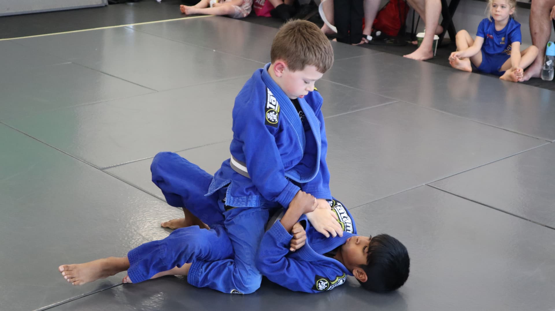 Two young kids in blue gis rolling at the Mat Shark in-house comp