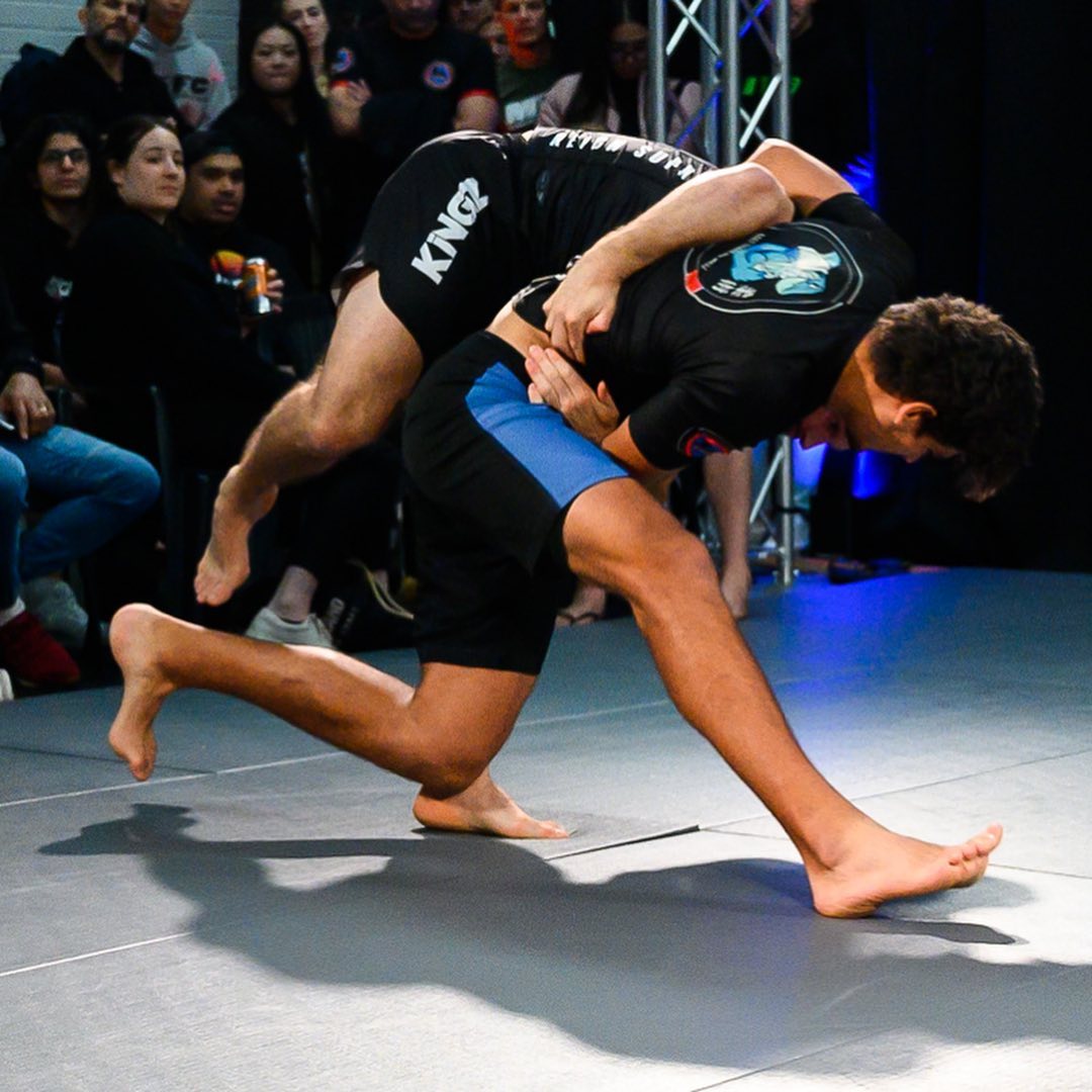 A Mat Shark athlete hitting a takedown in front of a crowd at a no-gi show