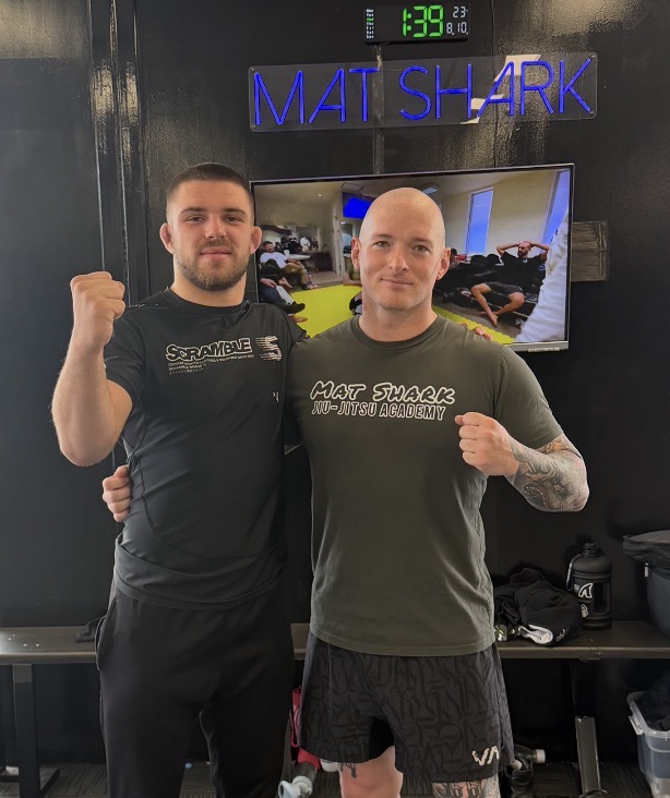 Two Mat Shark coaches under the neon academy sign