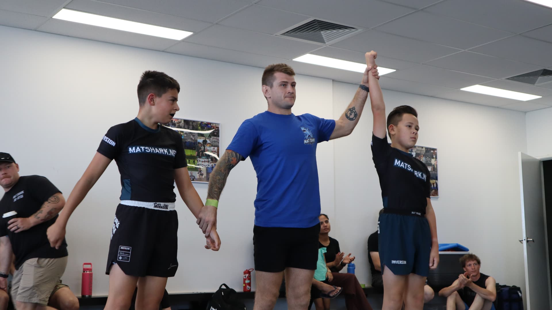 A coach raising a young student's hand at the Mat Shark in-house comp