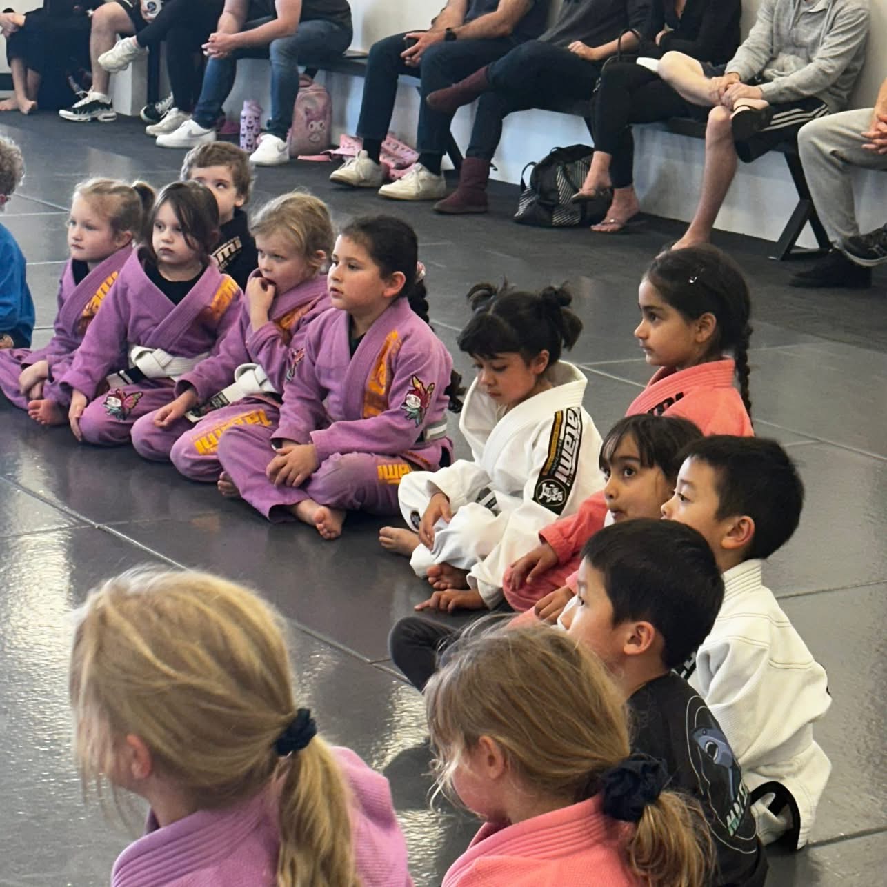Little kids sitting on the mats listening to their coach